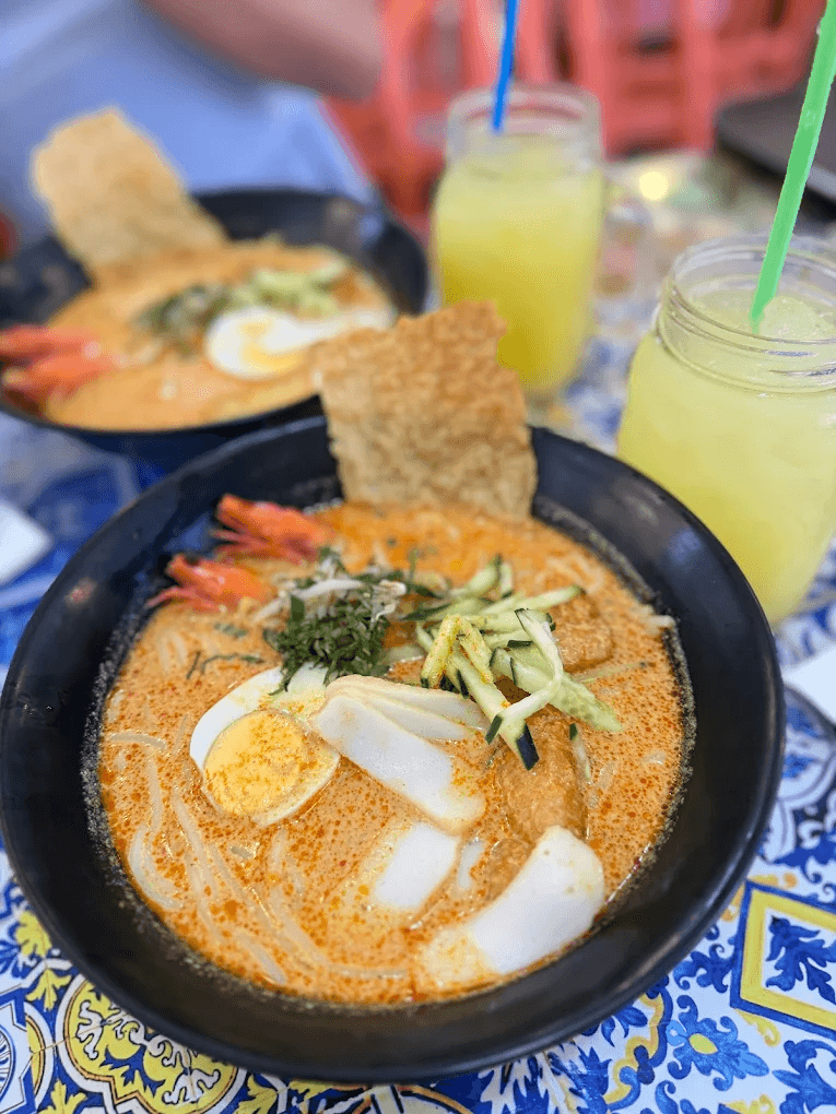 Bowl of rich coconut broth Sing Laksa and traditional Kueh Kueh at Leshan Cafe, delicious Telok Ayer food.